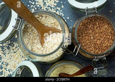 Cereali (farinata d'avena, grano saraceno, riso) in vasi di vetro in cucina. Concetto senza glutine. Varietà di cereali per la preparazione di cibi e pasti sani fatti in casa. Foto Stock