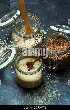 Cereali (farinata d'avena, grano saraceno, riso) in vasi di vetro in cucina. Concetto senza glutine. Varietà di cereali per la preparazione di cibi e pasti sani fatti in casa. Foto Stock