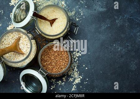 Cereali (farinata d'avena, grano saraceno, riso) in vasi di vetro in cucina. Concetto senza glutine. Varietà di cereali per la preparazione di cibi e pasti sani fatti in casa. Foto Stock