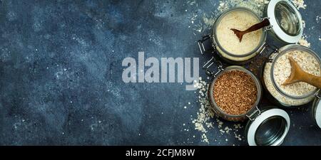 Cereali (farinata d'avena, grano saraceno, riso) in vasi di vetro sullo sfondo della bandiera della cucina. Concetto senza glutine. Varietà di cereali per rendere sano l'omema Foto Stock