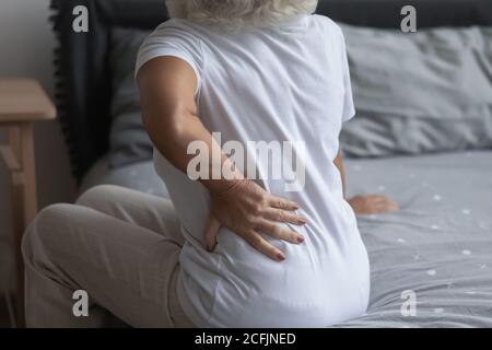 Primo piano donna matura malsana che si tocca dietro, seduto a letto Foto Stock