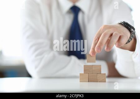 Uomo d'affari tiene in mano un cubo di legno e costruisce una piramide. Foto Stock