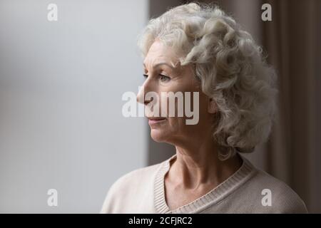 Primo piano sconvolto donna anziana matura che guarda fuori finestra Foto Stock