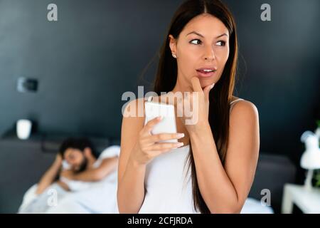 Donna che parla privatamente sul cellulare mentre suo marito dorme sopra letto Foto Stock