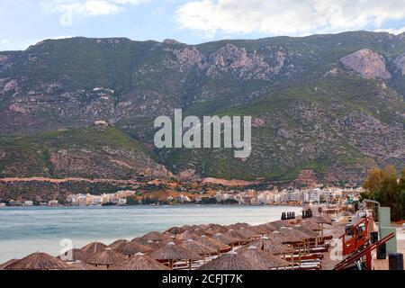 Vista delle cime di paglia di ombrelloni e lettini in legno con materassi sul lungomare desertato di Loutraki in Grecia. Foto Stock