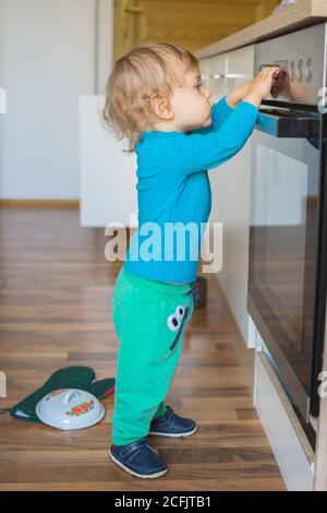 Bambino piccolo e curioso che gioca con le manopole del forno in cucina. Pericolo per i bambini incustoditi, prevenzione degli incidenti a casa phot concettuale Foto Stock