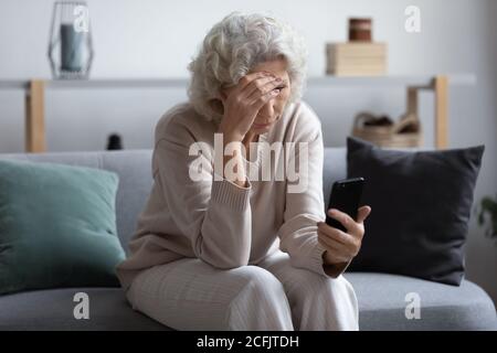 Infelice stressato donna di mezza età matura guardando lo schermo del telefono Foto Stock
