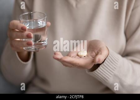 Primo piano donna matura che tiene un bicchiere d'acqua e pillola Foto Stock