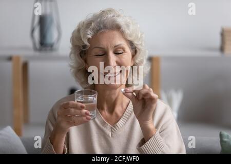 La testa ha girato sorridendo donna matura che tiene il vetro dell'acqua e la pillola Foto Stock