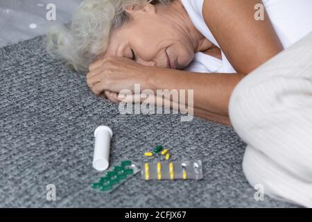 Primo piano depressa donna matura sdraiata a letto con meds Foto Stock