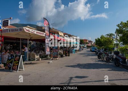 La strada che costeggia il lungomare della località turistica di Nydri, fiancheggiata da ristoranti, bar, caffetterie e negozi per i turisti. Foto Stock