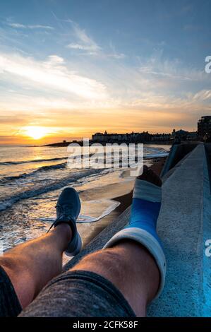 Maschio Sat sulla parete con getto a piedi godendo il tramonto al porthc awl Foto Stock