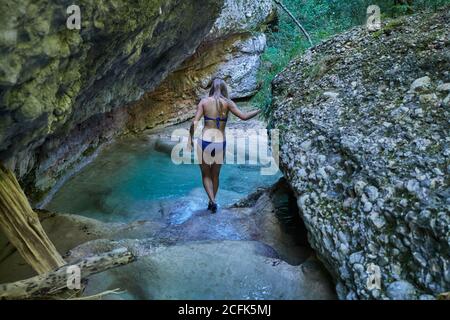 Vista posteriore di anonima donna in viaggio in bikini che attraversa il lago turchese Foto Stock