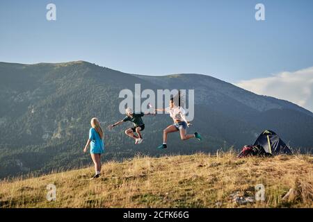 Compagnia di amici felici che saltano in collina in montagna mentre libertà durante le vacanze estive Foto Stock