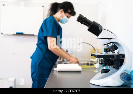 Microscopio moderno posto sul tavolo vicino al medico femminile in medicina maschera in laboratorio di clinica moderna Foto Stock