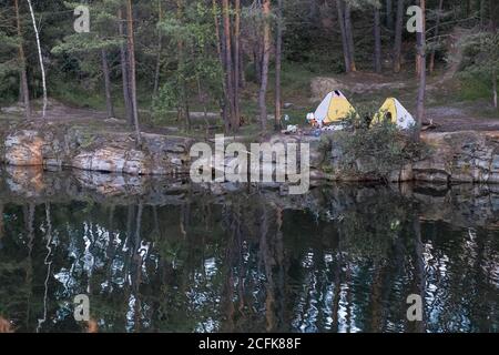 Campeggio sul lago. Vista delle tende turistiche situate ai margini di una cava di granito allagata tra alberi di pino Foto Stock