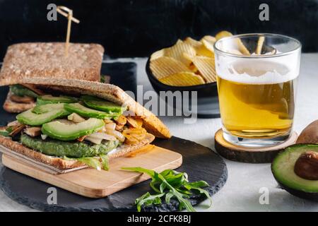 Gustoso sandwich con avocado posto sul tavolo con un bicchiere di birra e patatine al caffè Foto Stock