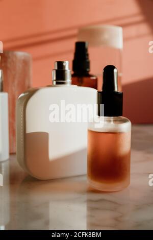 Flacone contagocce in vetro con siero da skincare collocato vicino al flacone spray e altri contenitori con prodotti cosmetici su tavola di marmo contro parete rosa Foto Stock