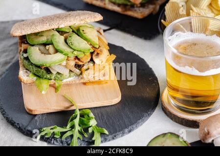 Gustoso sandwich con avocado posto sul tavolo con un bicchiere di birra e patatine al caffè Foto Stock