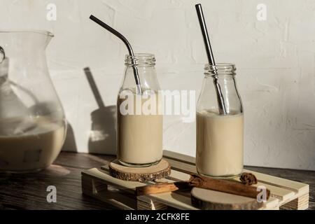 Bottiglie di vetro riempite con sana frullato dolce fatto in casa con cannella posto su tavolo di legno contro muro con ombra di monstera foglie Foto Stock