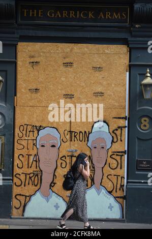 Londra, Regno Unito. 5 settembre 2020. Una donna cammina oltre il Garrick Arms Pub a Charing Cross Road rimane imbarcato, un murale dipinto con i lavoratori NHS. Foto Stock