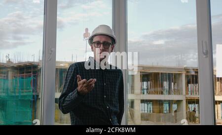 Medio shot.tecnico caucasico indossando cappello bianco di sicurezza che parla con la macchina fotografica. Riprese professionali con risoluzione 4K. 025. Può essere utilizzato, ad esempio, nel suo commercio Foto Stock