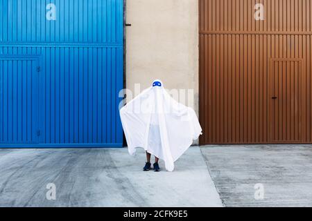 bambino senza volto in costume fantasma bianco spaventoso con le braccia distese Mentre si è in città durante Halloween Foto Stock