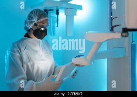 Professionista medico in uniforme medica e maschera protettiva con occhiali di protezione mentre si utilizzano le moderne apparecchiature diagnostiche in ospedale Foto Stock