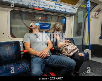 I passeggeri sulla carrozza del treno sotterraneo di Londra indossano una copertura facciale e cercano di praticare l'allontanamento sociale. Foto Stock