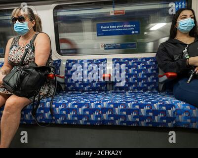 I passeggeri sulla carrozza del treno sotterraneo di Londra indossano una copertura facciale e cercano di praticare l'allontanamento sociale. Foto Stock