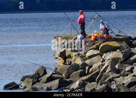 Rod pescatori su un molo nel fiume Cree estuario guardando dal litorale di Carsluith verso il Machars, Dumfries & Galloway, Scozia. Il mare aperto è fuori di colpo a sinistra. Foto scattata a settembre 2020. Foto Stock