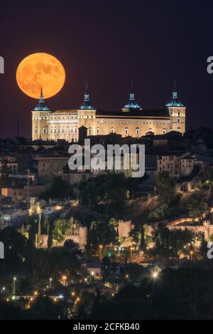 Splendida vista sulla luna piena e luminosa nel cielo notturno scuro sopra la città vecchia con il palazzo storico incandescente Foto Stock