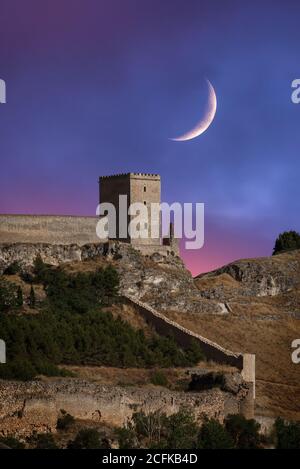 Maestoso scenario con la luna nel cielo di sera sulle rovine di antica fortezza in pietra situata su una collina in un terreno montano desertico Foto Stock