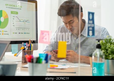 Uomo d'affari che lavora in ufficio domestico con distanza sociale utilizzando la partizione dello schermo per evitare la diffusione del coronavirus COVID-19. Nuovo concetto normale afte Foto Stock