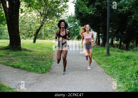 Corpo pieno di giovani amici multirazziali in sportswear jogging sul sentiero nel parco durante l'allenamento insieme in estate giorno Foto Stock