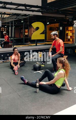 Positivo giovane uomo e donne in abbigliamento sportivo che si rompono e. chiacchierare durante l'allenamento in palestra moderna Foto Stock