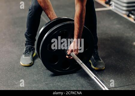 Crop anonimo atleta maschile in abbigliamento sportivo mettendo piatti pesanti su barbell mentre si prepara per l'allenamento di sollevamento pesi in palestra Foto Stock