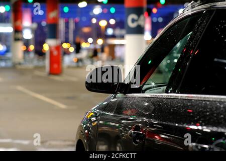 Lo specchietto laterale della vettura è coperto da gocce di pioggia. L'auto è parcheggiata in un angolo buio del parcheggio Foto Stock
