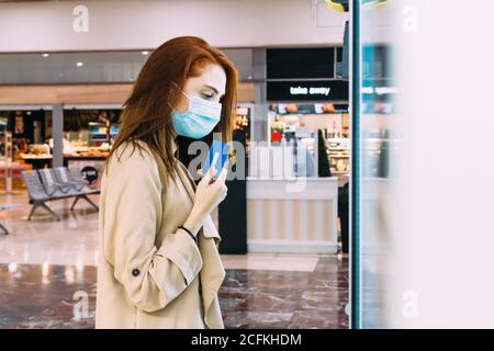 donna con una maschera facciale usa la sua carta di credito a. paga al distributore automatico Foto Stock