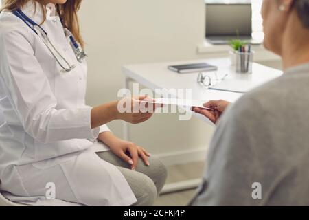 Il medico dà al paziente una prescrizione mentre si siede sul posto di lavoro nell'ufficio di una clinica medica. Foto Stock