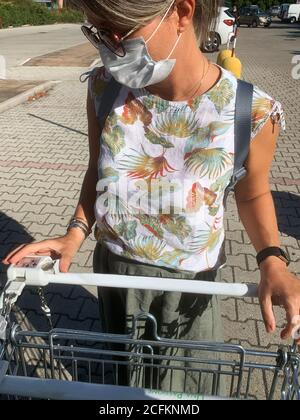 Covid-19. Donna che indossa una maschera protettiva per il viso prendendo il carrello al supermercato. Foto Stock