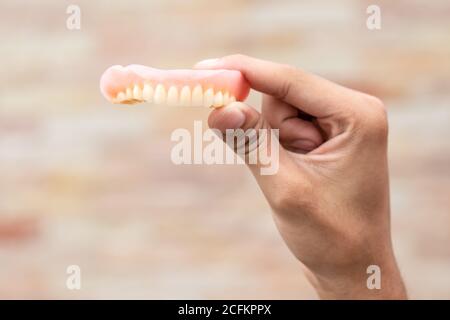 Un uomo sta tenendo le dentiere nelle sue mani. Protesi rimovibili flessibili. Denti falsi. Foto Stock