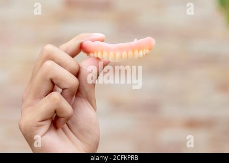 Un uomo sta tenendo le dentiere nelle sue mani. Protesi rimovibili flessibili. Denti falsi. Foto Stock