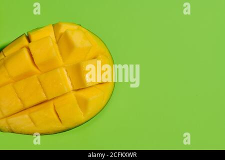 Dall'alto, primo piano di mango fresco maturo succoso a metà fette in pezzi su sfondo verde brillante Foto Stock