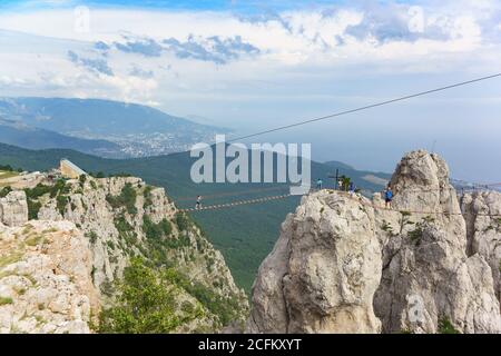 Mishor, Yalta, Crimea, Russia - 14 settembre 2018: Donne e uomini camminano su un ponte di corda teso tra i denti del monte ai-Petri. Un popolare touri Foto Stock