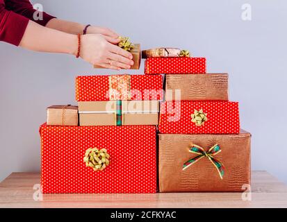 Vista di dettaglio delle mani della persona di donna che impilano i regali di Natale in un mucchio. Preparazione per il concetto di Natale. Foto Stock