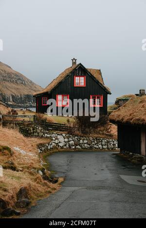 Casa residenziale in legno in insediamento in autunno sulle Isole Faroe sulle montagne innevate Foto Stock