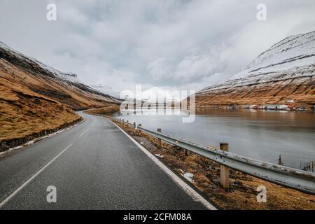 Spettacolare vista della strada tortuosa bagnata situata vicino al fiume e. Pendio di montagna con erba secca in inverno sulle Isole Faroe Foto Stock