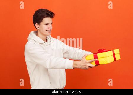 Profilo ritratto di giovane sorridente in felpa casual con cappuccio che tiene fuori la scatola presente, servizio di consegna espresso. Studio al coperto isolato Foto Stock