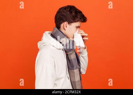 Profilo ritratto di giovane uomo in felpa casual con sciarpa a scacchi sul collo soffia il naso in tovagliolo, allergia stagionale. Isolamento delle riprese in studio al coperto Foto Stock